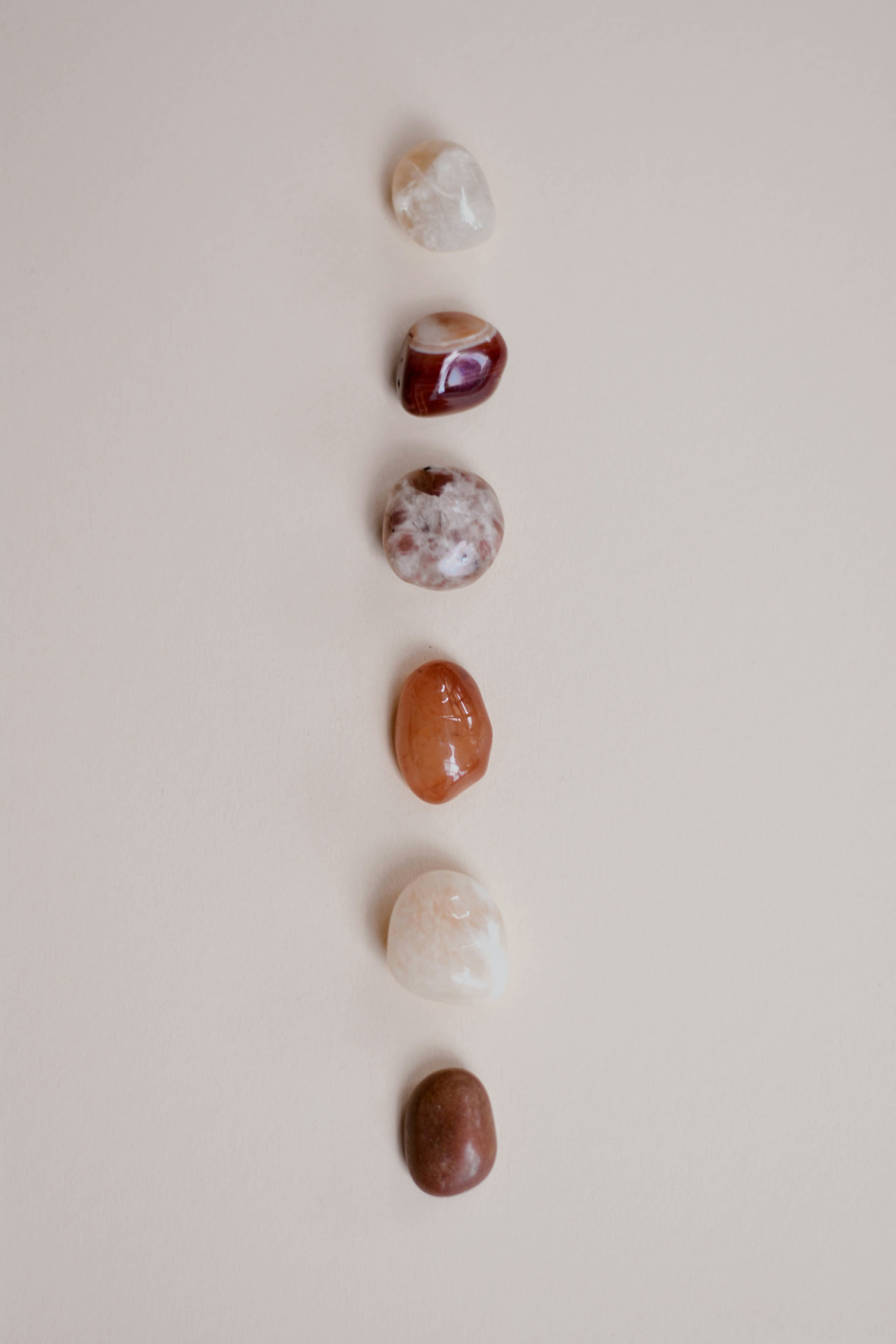 Row of polished healing stones arranged vertically on a soft blush background